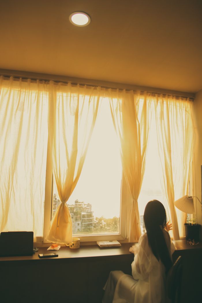Crafting Captivating Headlines: Your awesome post title goes here Silhouette of a woman looking out a sunlit window with soft curtains on a calm day inside.